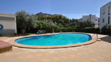 Una piscina con solárium de baldosas, rodeada de vegetación y edificios.