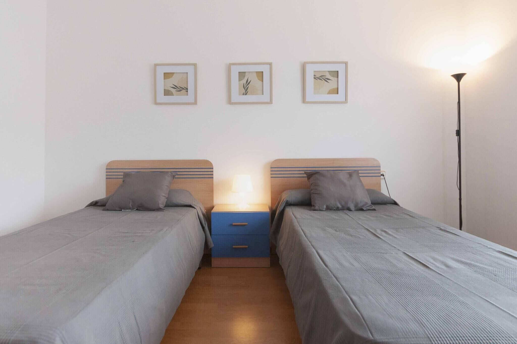 Une chambre double avec deux lits simples, une table de chevet avec une lampe et trois tableaux encadrés au mur.