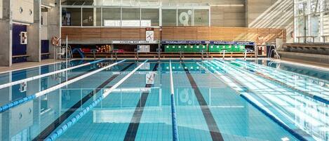 A large indoor swimming pool with multiple lanes, wooden ceiling beams, and a clear view of the pool area.
