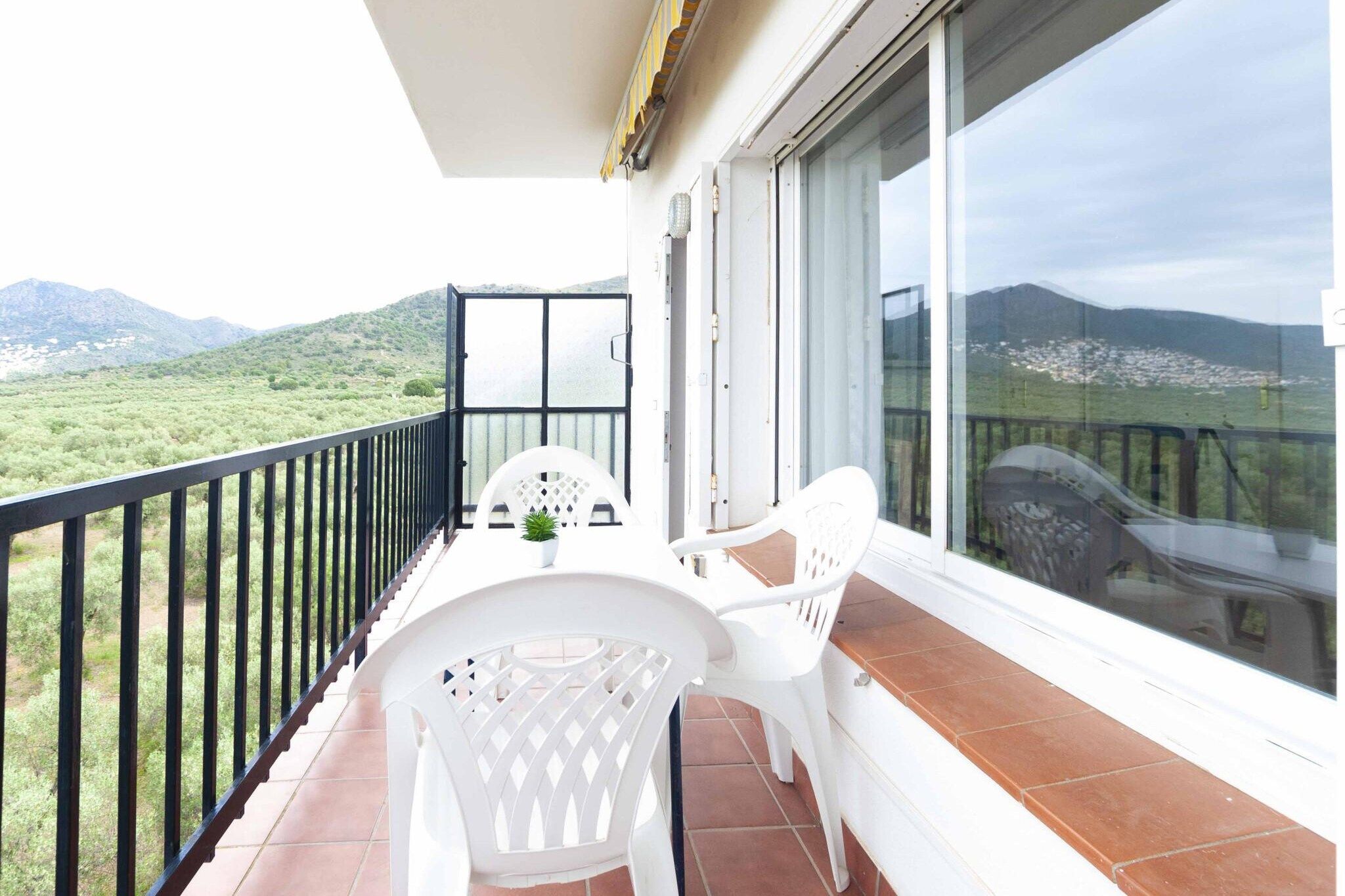 A balcony with a table and chairs, a potted plant, and a view of a mountainous landscape.
