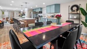 A modern kitchen with teal cabinets, a central island, and a dining area with a black table and colorful placemats.