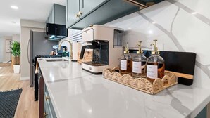A modern kitchen with a marble countertop, a coffee machine, and three bottles of condiments.