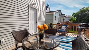 A patio with a glass table, wicker chairs, and a barbecue grill.