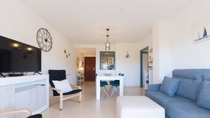 Un saló modern amb televisió, un sofà, una zona de menjador amb taula i cadires, i una cuina al fons.