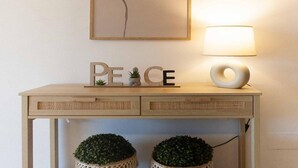 Una taula consola de fusta amb un cartell que diu 'PEACE', una làmpada i dues plantes en testos.
