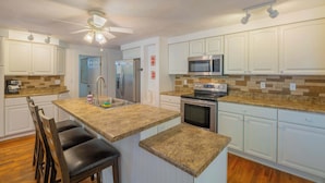 A kitchen with white cabinets, a granite countertop, a stainless steel refrigerator, a microwave, and an oven.