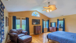A bedroom with a wooden floor, a large bed, a leather sofa, a dresser, and a ceiling fan.