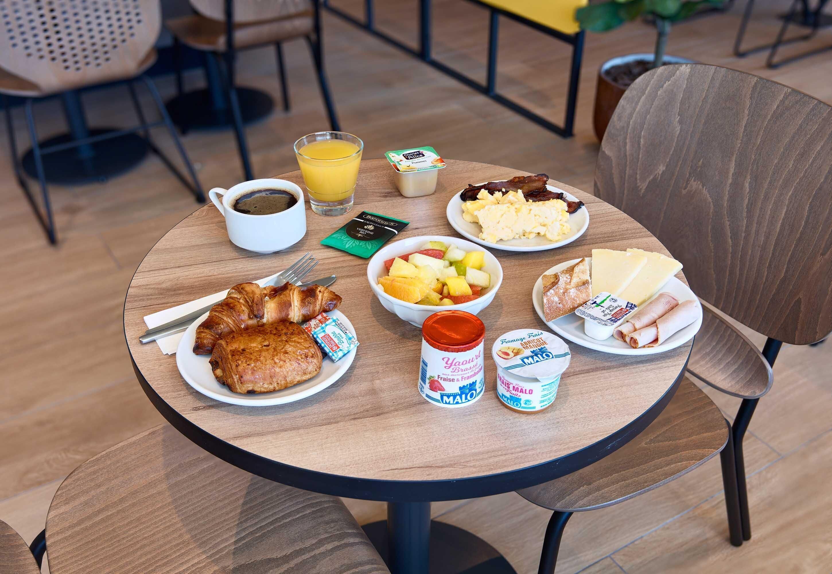 Mesa de café da manhã com croissants, ovos, bacon, frutas e iogurtes em camadas.