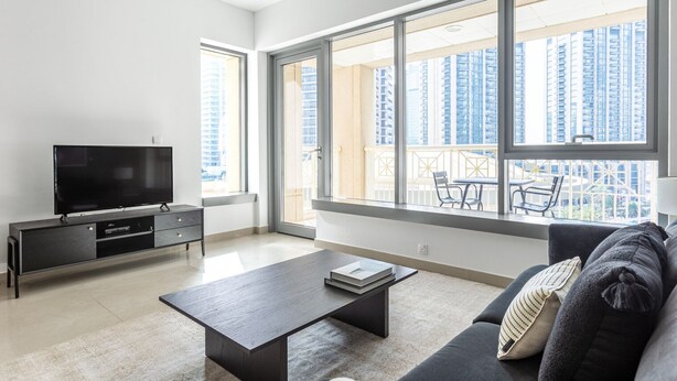 A modern living room with a flat-screen TV, a dark coffee table, and a sofa with cushions. Large windows offer a view of high-rise buildings. - Blueground | Downtown Dubai, pool, nr Burj Khalifa (Dubai)