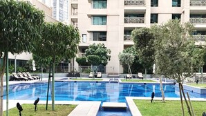 A swimming pool with a geometric pattern, surrounded by grass and trees, with a building in the background. - Blueground | Downtown Dubai, pool, nr Burj Khalifa (Dubai)