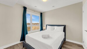 A bedroom with a bed, a window with curtains, a nightstand, and a lamp. - Stylish Niagara Falls Getaway with Rooftop City Views (Niagara Falls)