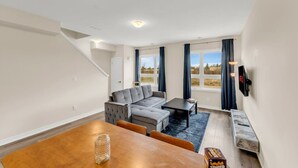 A modern living room with a sectional sofa, a dining table, and a TV mounted on the wall. - Stylish Niagara Falls Getaway with Rooftop City Views (Niagara Falls)