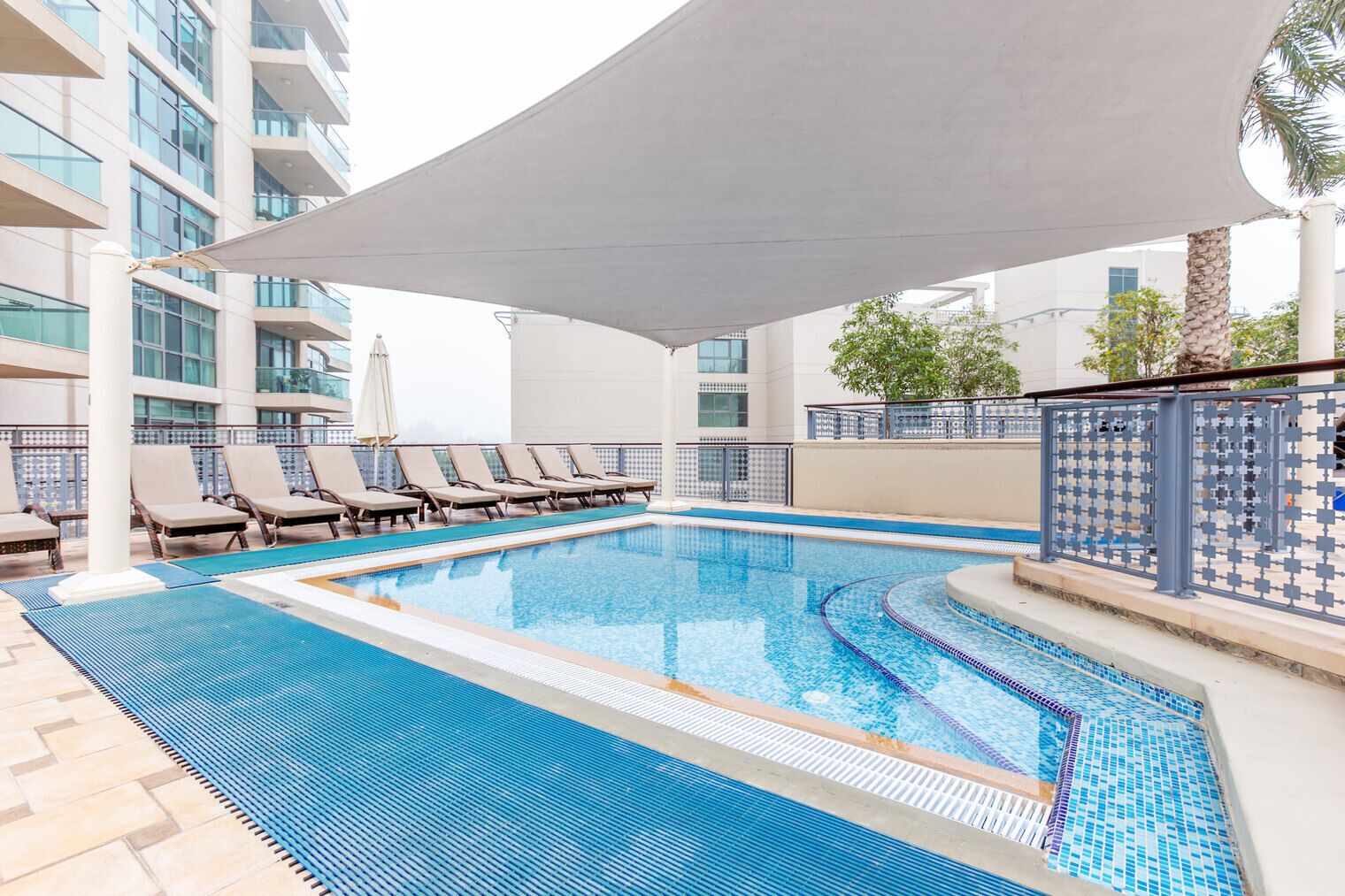 Ein Pool mit Liegestühlen und einem schattigen Bereich, umgeben von einem modernen Gebäude mit Balkonen.