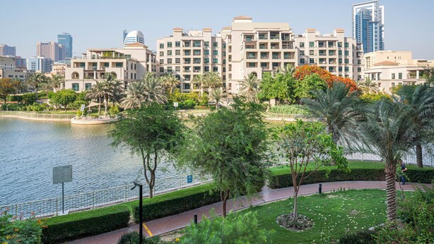A waterfront hotel with a view of the city skyline, a garden with palm trees, and a pathway along the water. - Blueground | The Views, pool, nr Canal (Dubai)