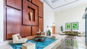 A modern lobby with a large wooden panel wall, a seating area with sofas and a coffee table, and two framed abstract paintings on the wall. - Blueground | The Views, pool, nr Canal (Dubai)