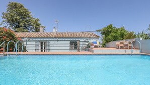 Une piscine avec une terrasse carrelée, un petit bâtiment doté d’un toit en tuiles et des chaises longues.