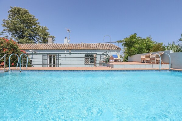 A swimming pool with a tiled deck, a small building with a tiled roof, and lounge chairs.