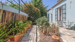 Un étroit couloir extérieur agrémenté de plantes en pot, d’une clôture en bambou et d’un bâtiment doté d’une terrasse carrelée et d’une table.