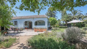 Une maison avec un toit en tuiles, une terrasse avec des chaises et une table, et un jardin avec différentes plantes.