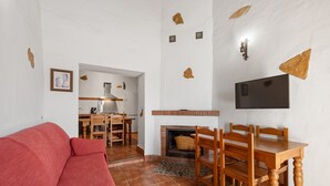 Una sala de estar con sofá rojo, mesa de comedor de madera, sillas, chimenea y televisor de pantalla plana montado en la pared.
