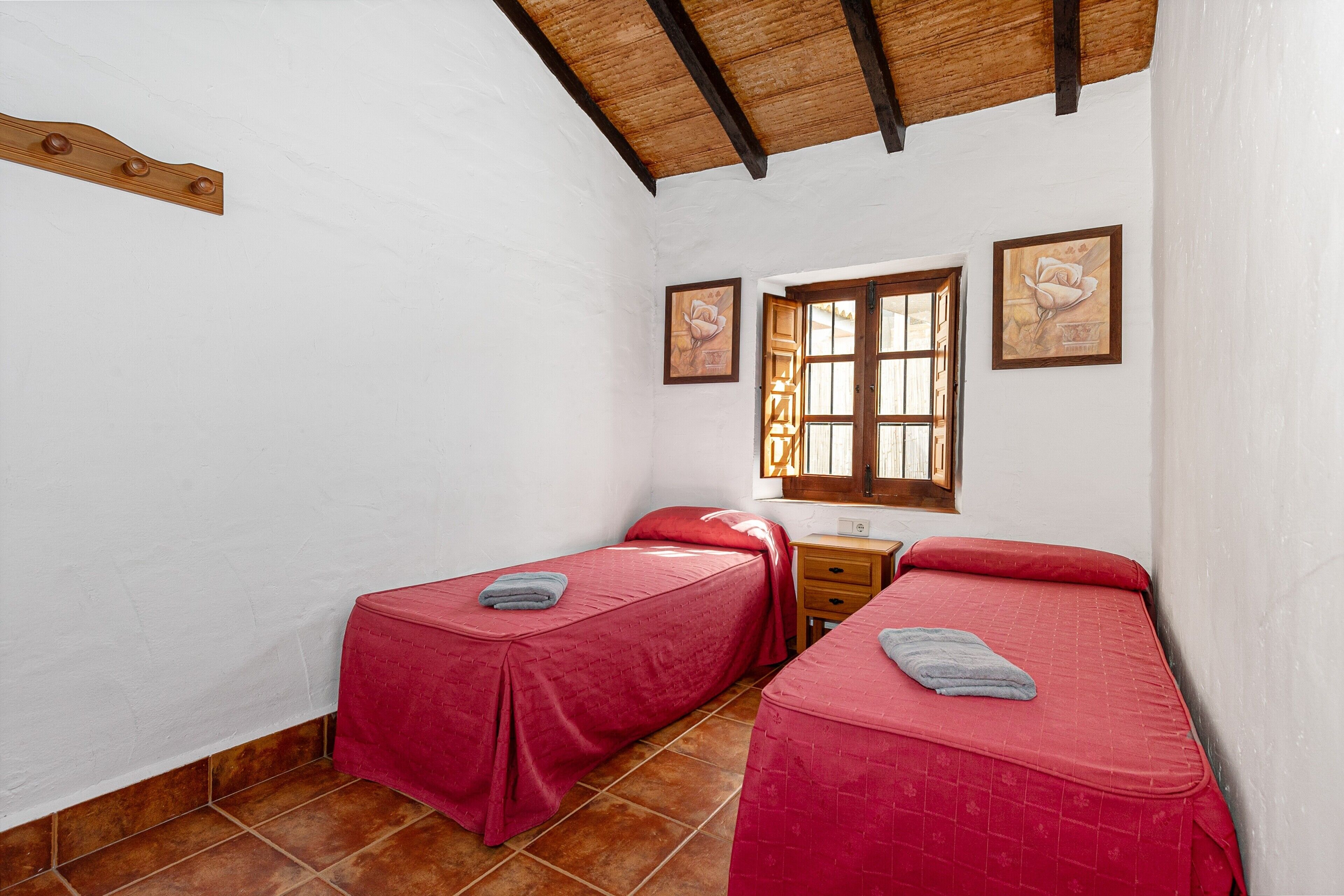 Una habitación con dos camas, techo de madera, paredes blancas y ventana con vistas.