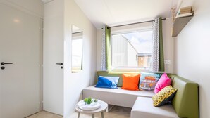 Una habitación con ventana, un sofá con cojines de colores, una mesita con una planta y una puerta.