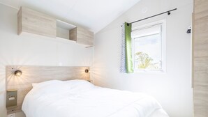 Un dormitorio moderno con cama, iluminación empotrada, una ventana con cortina y una estantería fijada a la pared.