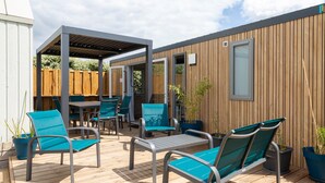 Un porche techado al aire libre con muebles de metal, terraza de madera y una pared de madera con una ventana.