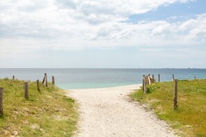 Un sentier sablonneux menant à une plage, avec une clôture de chaque côté.