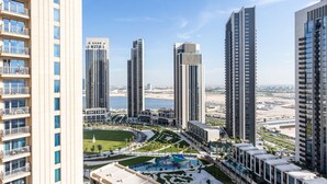 Un edificio residencial de gran altura con varios balcones, una piscina rodeada de jardines y vistas a una ciudad costera.