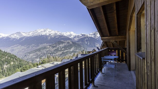 A wooden balcony with a table and chairs, overlooking snow-capped mountains. - Nice apt near the slopes for 6 pers (Modane)