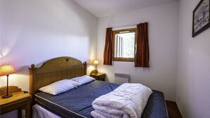 A single bed with a wooden headboard, a bedside table with a lamp, a window with curtains, and a wall-mounted picture frame. - Nice apt near the slopes for 6 pers (Modane)