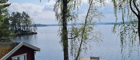 A cabin with a deck and a dock extending into a calm lake, surrounded by trees and a clear sky.