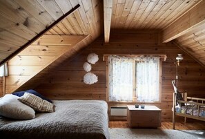 Ein gemütliches Schlafzimmer im Dachgeschoss mit schrägen Wänden, einem Bett mit Quilzdecke, einem Nachttisch, einer Kommode und einem Fenster mit Vorhängen.