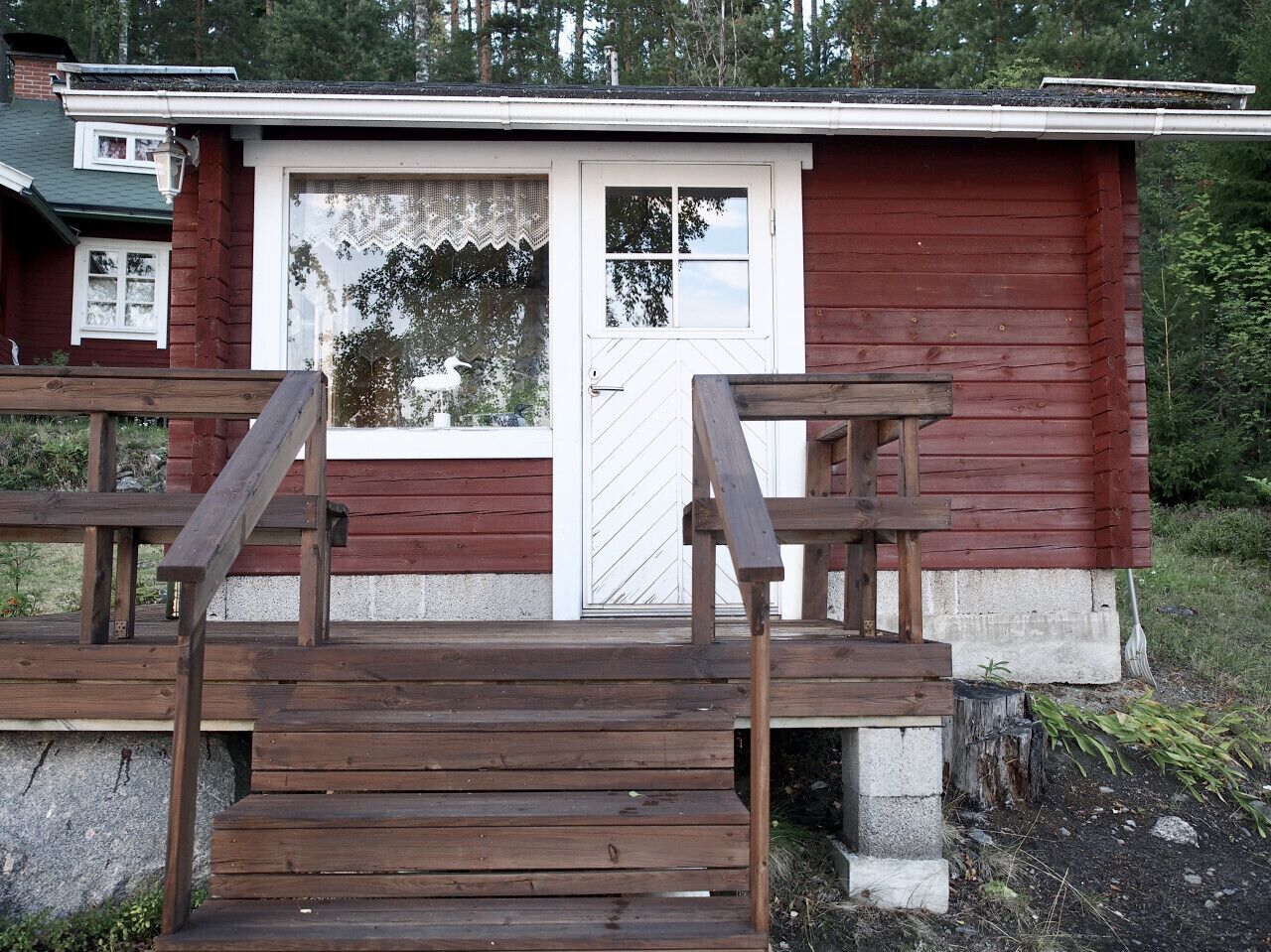 Eine Holzterrasse führt zu einer roten Holzhütte mit einer weißen Tür und Fenstern.