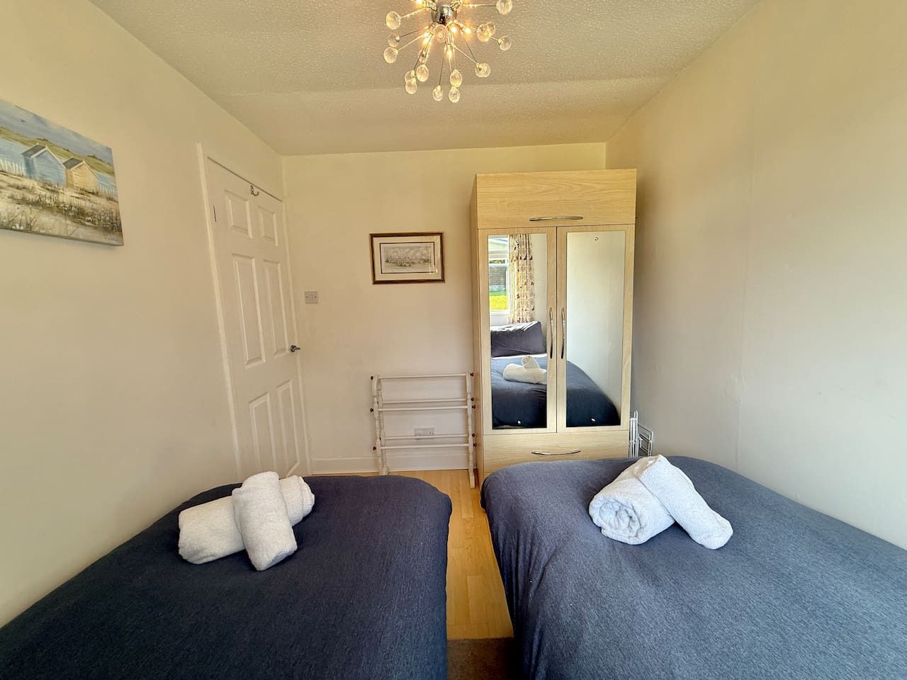 A room with two beds, a wooden wardrobe, a white radiator, and a door leading to another room.