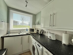 A modern kitchen with a washing machine, microwave, toaster, and kettle.