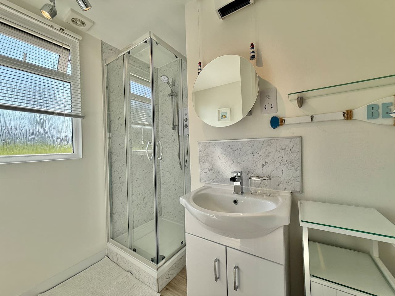 Un baño moderno con cabina de ducha de vidrio, un lavamanos blanco y un salpicadero de mármol.