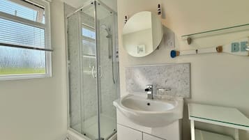 Un baño moderno con cabina de ducha de vidrio, un lavamanos blanco y un salpicadero de mármol.