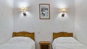 A room with two single beds, a small wooden nightstand, and two wall-mounted lamps. - 40m from ski slopes, 3rd floor, view ski slopes, fitness, swimming pool, sauna, balcony, tv (Les Orres)