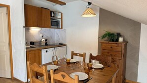 A dining area with a wooden table and chairs, a kitchen with wooden cabinets and a microwave, and a ceiling light fixture. - 40m from ski slopes, 3rd floor, view ski slopes, fitness, swimming pool, sauna, balcony, tv (Les Orres)