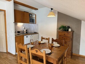 Ruokailutila, jossa on puinen pöytä ja tuolit, keittiö, jossa on puiset kaapit ja mikroaaltouuni, sekä kattovalaisin.