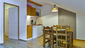 A compact kitchen with wooden cabinets, a microwave, and a dining table with chairs. - 40m from ski slopes, 3rd floor, view ski slopes, fitness, swimming pool, sauna, balcony, tv (Les Orres)