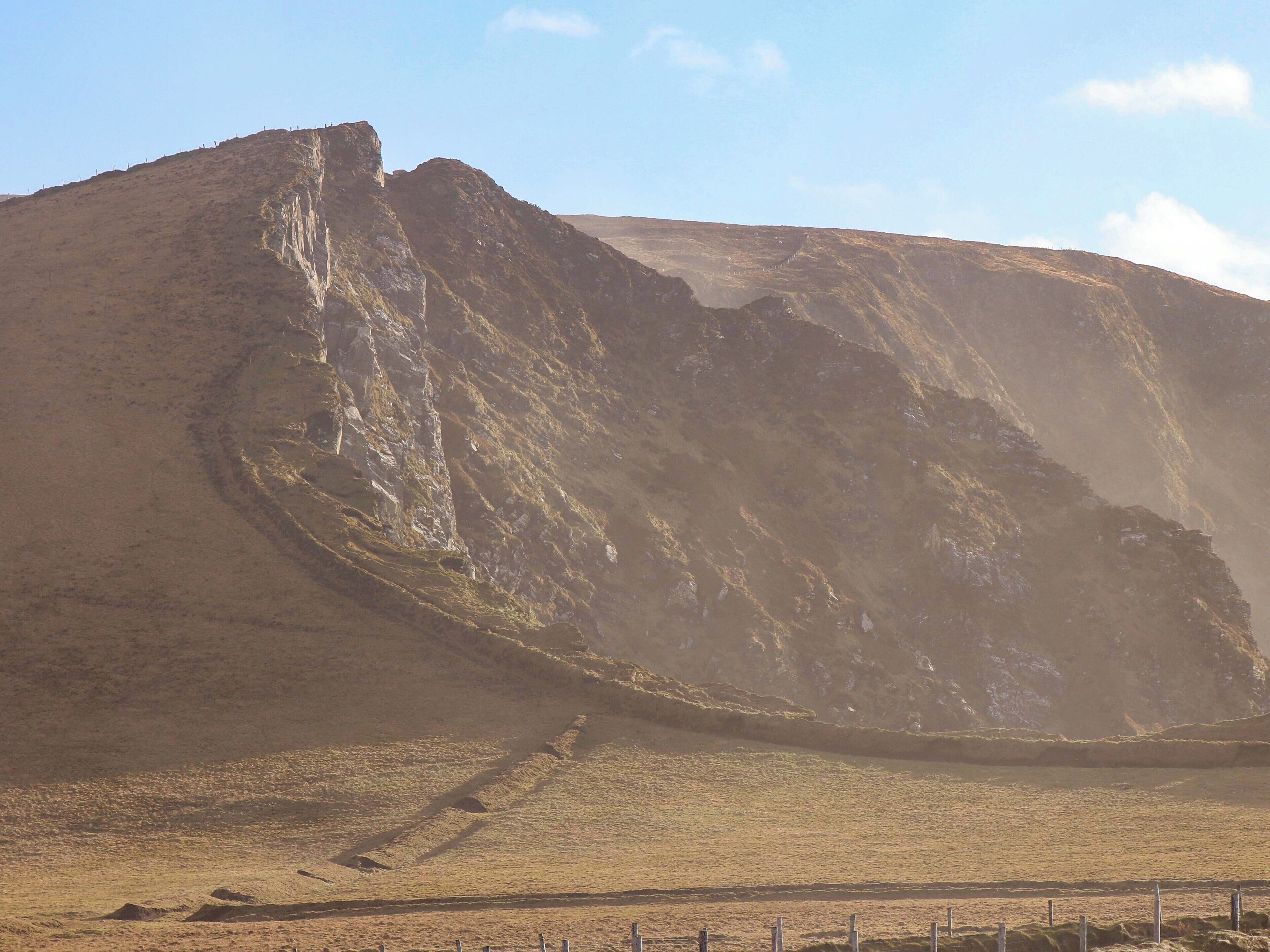 A rugged mountain landscape with a dirt path leading up to a rocky outcrop.