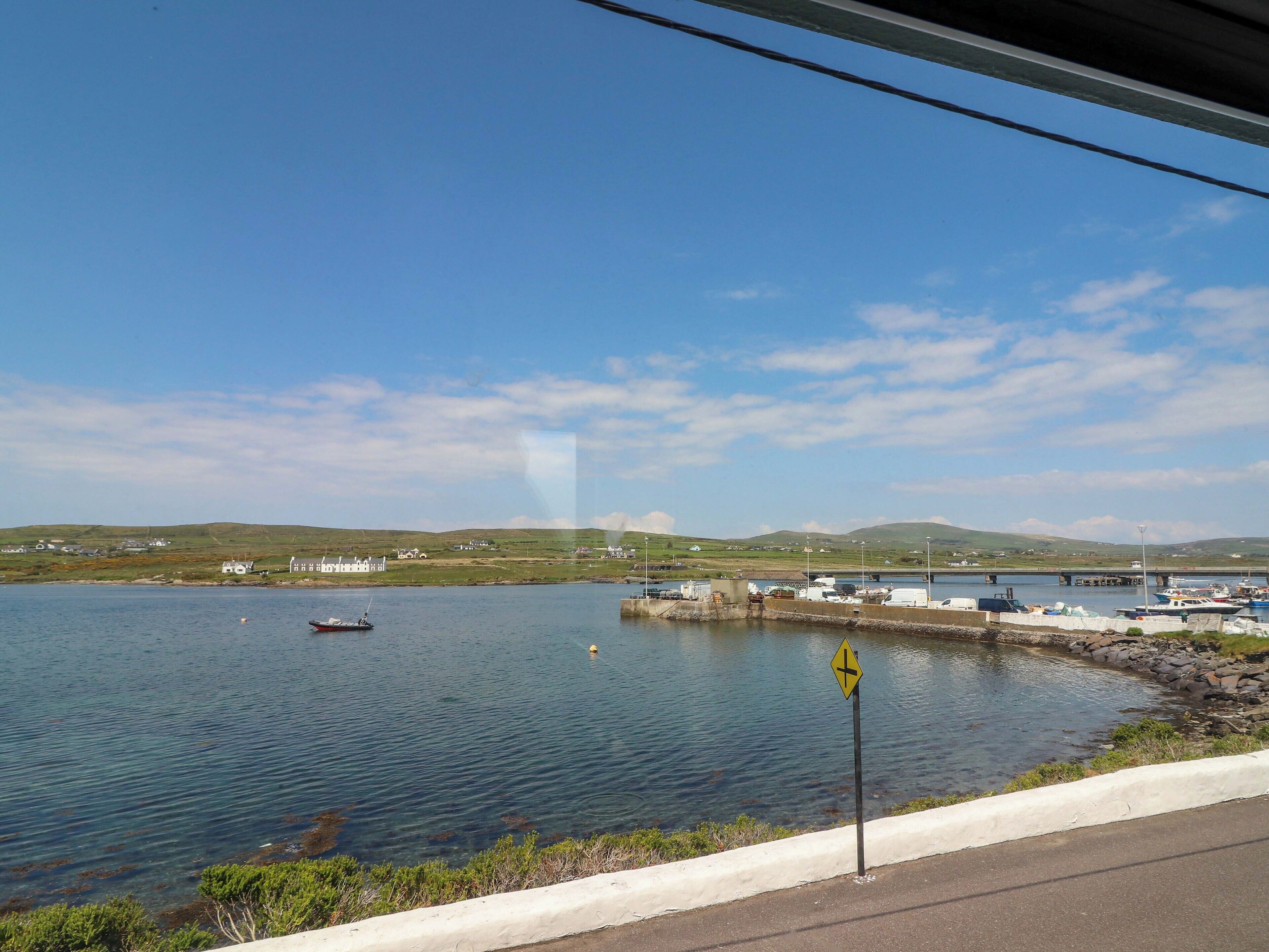 A coastal road with a clear view of a marina, boats, and a bridge in the distance.
