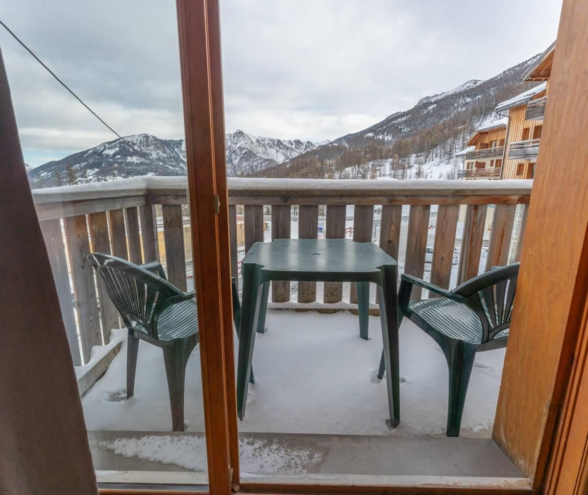 Un balcon avec une table et des chaises, donnant sur un paysage montagneux enneigé.