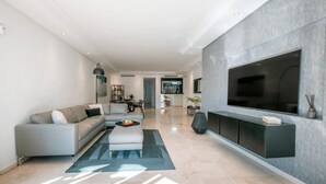 A modern living room with a grey sofa, a coffee table, and a large TV mounted on the wall. - Luxury Beachfront Heated Pool & SPA & GYM–EHHouse (Loma Del Monte)