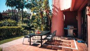 An outdoor patio with a table and chairs, surrounded by lush greenery and palm trees. - Luxury Beachfront Heated Pool & SPA & GYM–EHHouse (Loma Del Monte)