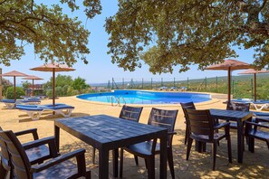 Un área junto a la piscina con sillones de descanso, sombrillas y mesas.