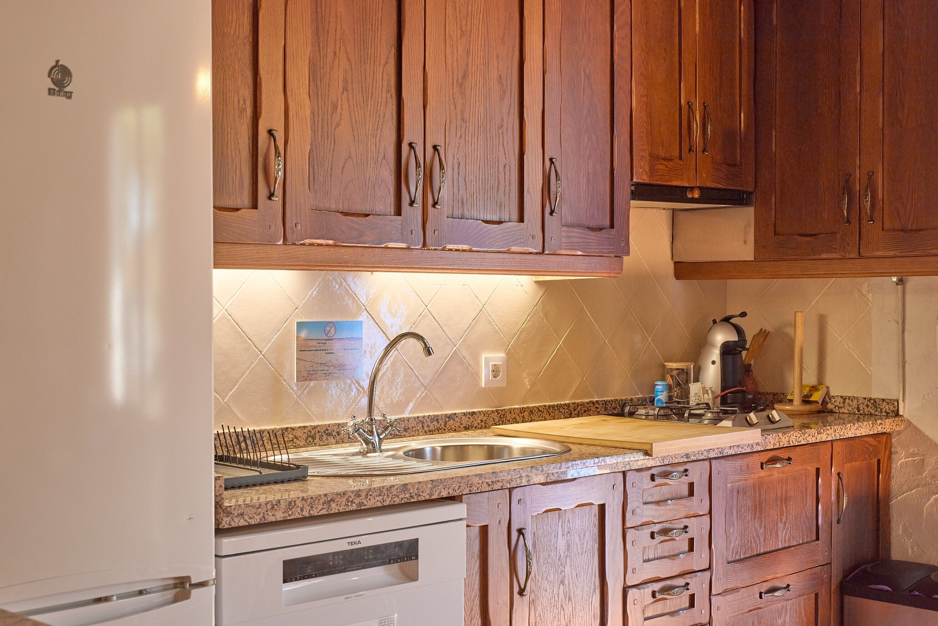 A kitchen with wooden cabinets, a stainless steel sink, a white dishwasher, and a granite countertop.